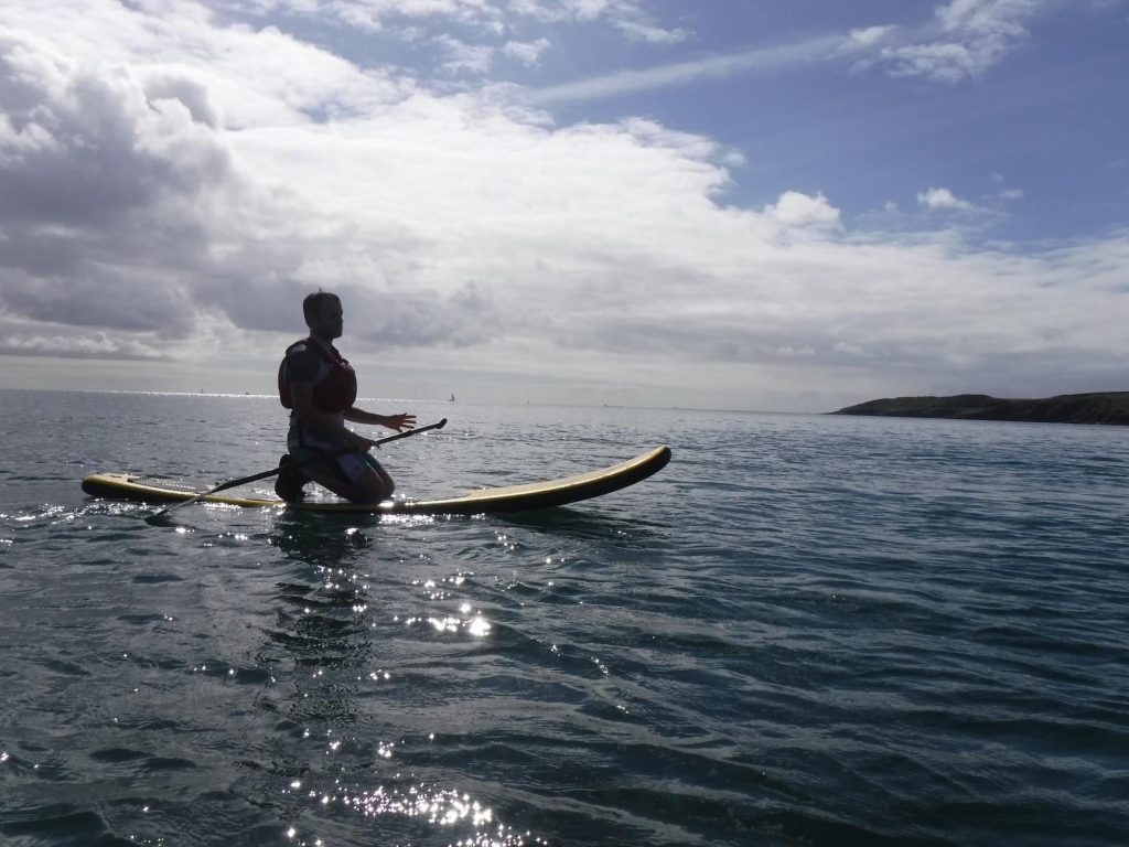 Silouette of a man kneeling on a paddleboard in the ocean
